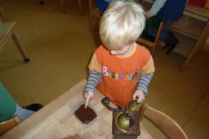 ein Kind steht am Tisch und prüft mit dem Finger den gemahlenen Kaffee